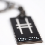 Park in the Sky enamel keychain with the High Line railroad-track "H" icon and "Park in the Sky, New York NY" in all caps, shown closeup, with the tagline in focus.