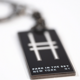 Park in the Sky enamel keychain with the High Line railroad-track "H" icon and "Park in the Sky, New York NY" in all caps, shown closeup, with the tagline in focus.
