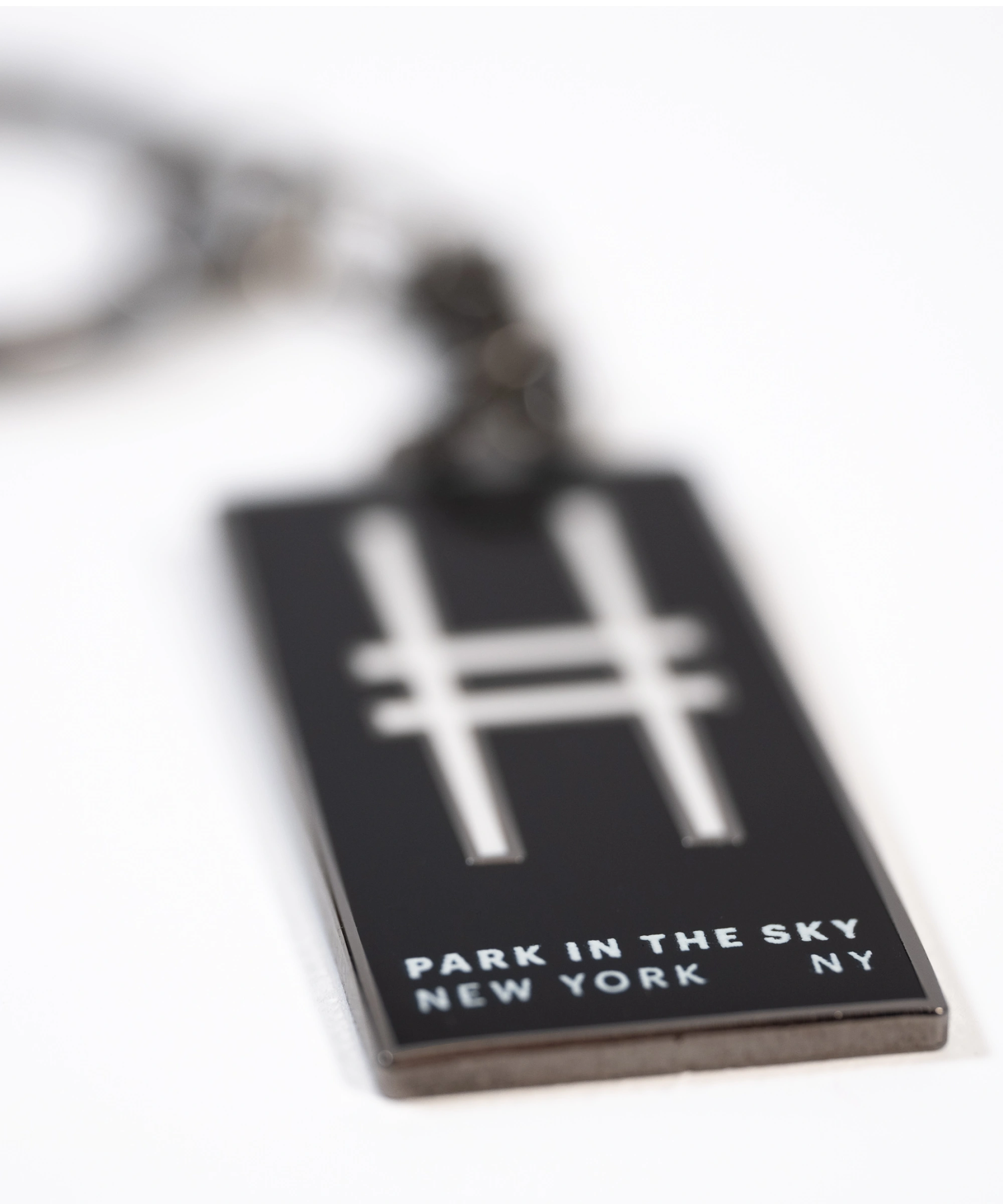 Park in the Sky enamel keychain with the High Line railroad-track "H" icon and "Park in the Sky, New York NY" in all caps, shown closeup, with the tagline in focus.
