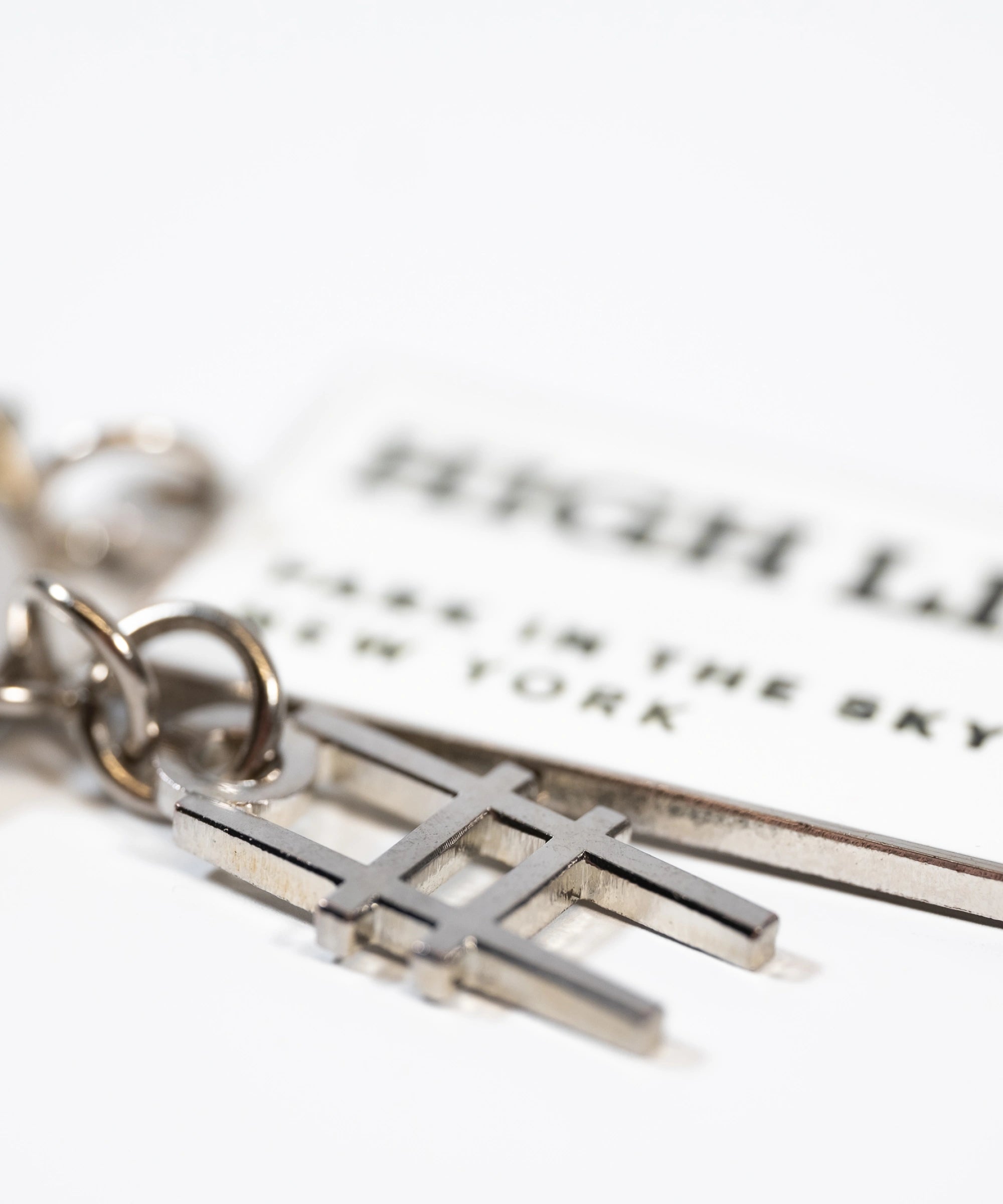 Closeup of the High Line Tag Keychain, featuring a small charm of the High Line railroad-track "H" icon in focus, with the enamel tag out of focus.