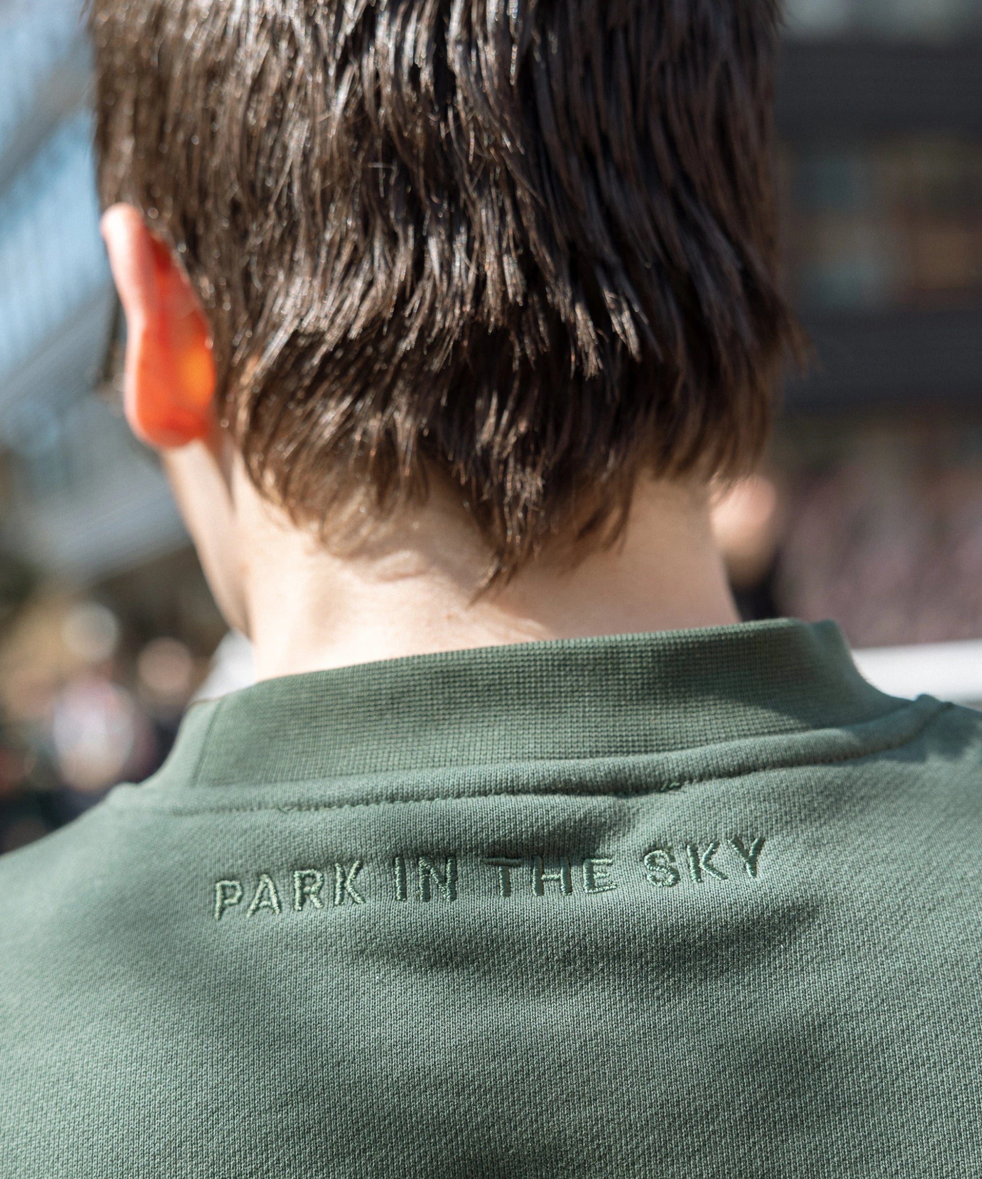 Close-up of "Park in the sky" neck embroidery detail. Person wears Big Icon Crewneck in Ivy while on the High Line.