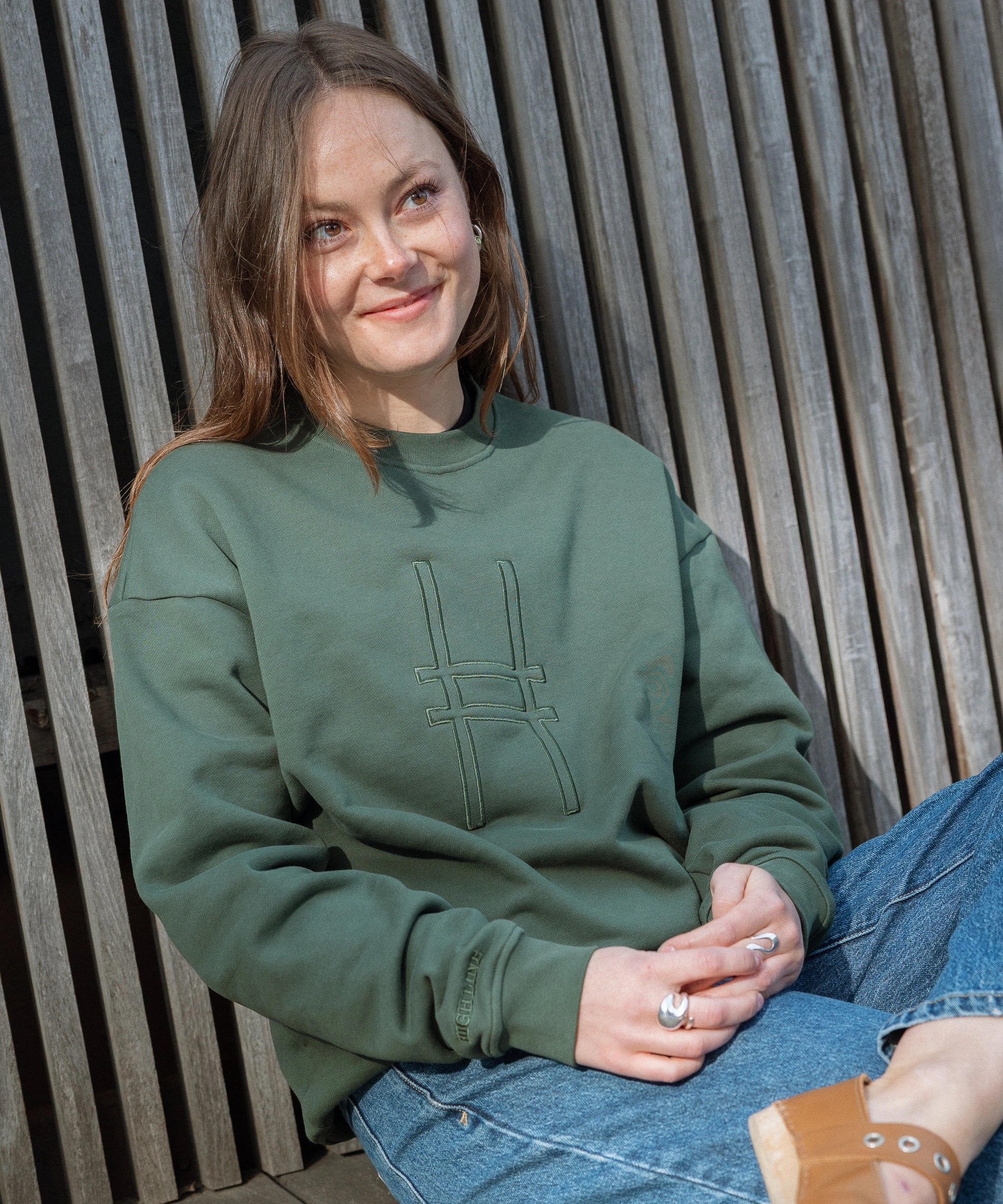 Woman wearing Big Icon Crewneck in Ivy with monochromatic embroidery details. Front features big High Line icon and High Line wordmark on sleeve. 