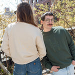 Two people, each wearing the Big Icon Crewneck and standing on the High Line. The person wearing the Ivy sweatshirt looks at the camera, hands in their pockets.