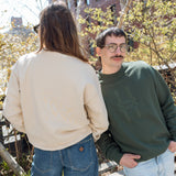 Two people, each wearing the Big Icon Crewneck and standing on the High Line. The person wearing the Ivy sweatshirt looks at the camera, hands in their pockets.