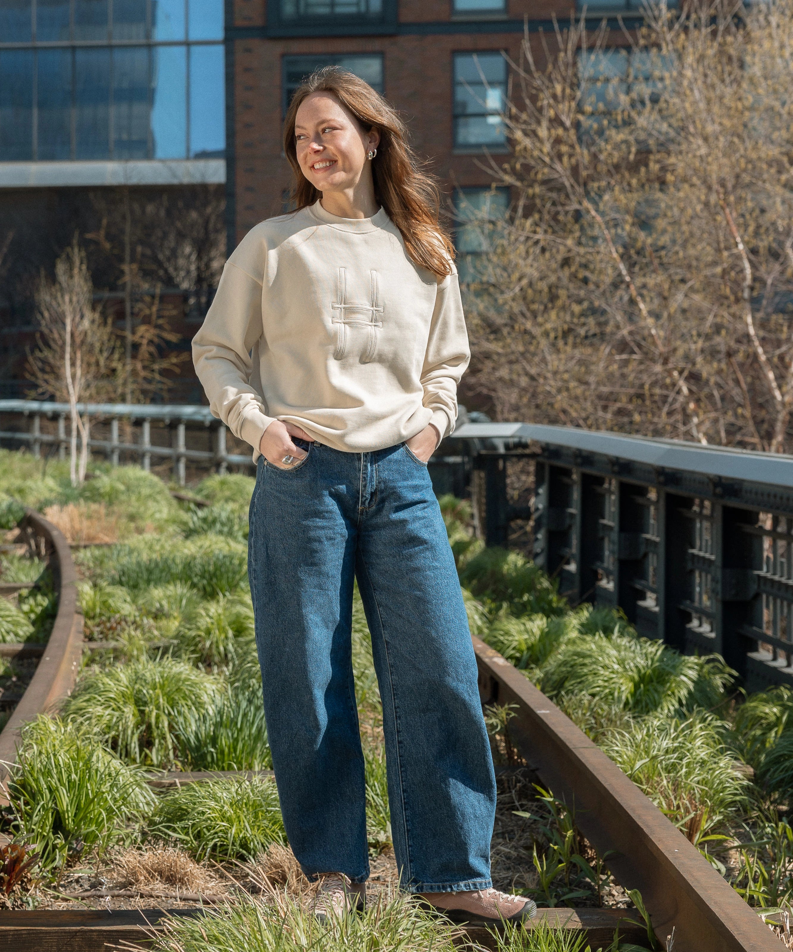 Woman standing on the High Line and wearing the Big Icon Crewneck in River Birch.