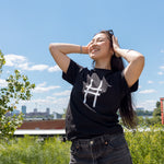 Woman wearing the High Line Icon Tee in black and pushing her sunglasses back in the sun.