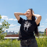 Woman wearing the High Line Icon Tee in black and pushing her sunglasses back in the sun.