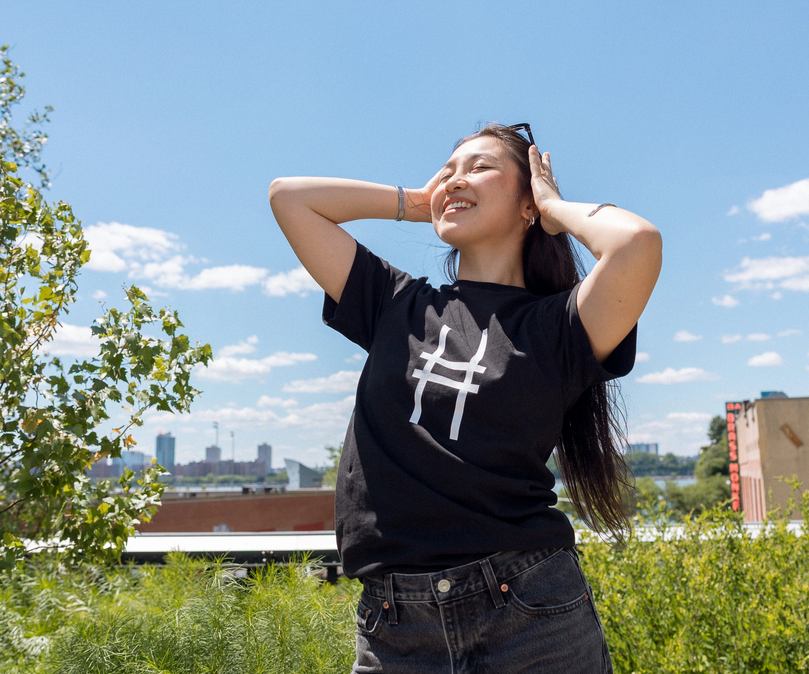 Woman wearing the High Line Icon Tee in black and pushing her sunglasses back in the sun.