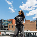 Woman wearing the High Line Icon Tee in black against the blue sky and view from the High Line.