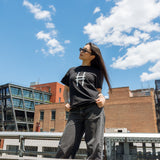 Woman wearing the High Line Icon Tee in black against the blue sky and view from the High Line.