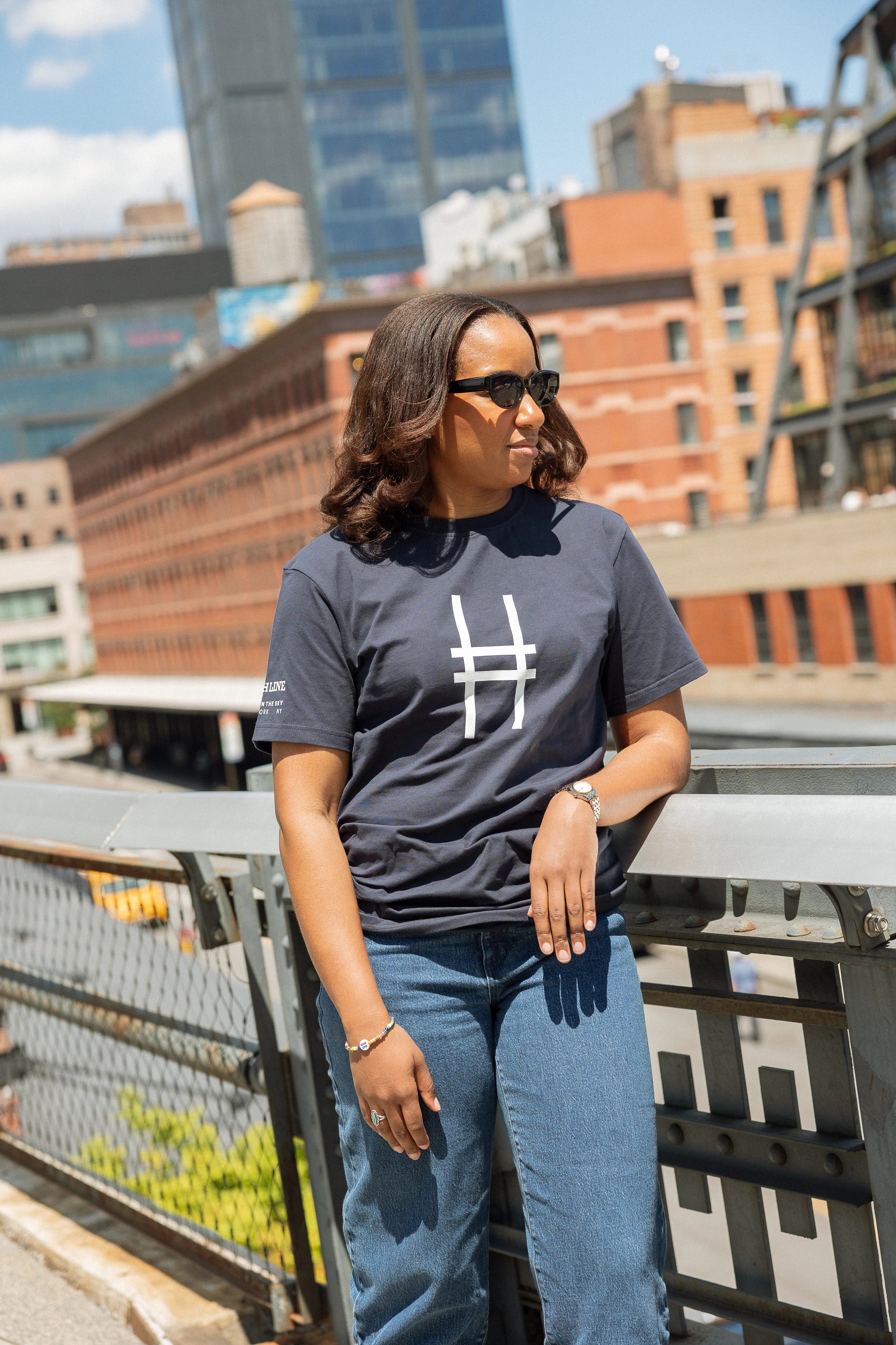 Woman wearing the High Line Icon Tee in navy and leaning against the railing of the High Line.