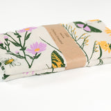 Claudia Pearson x High Line Chelsea Grassland tea towel, folded and wrapped in a kraft paper band. The flour sack cotton tea towel is covered in illustrations of butterflies and flowers that populate the High Line in green, yellow, and violet.