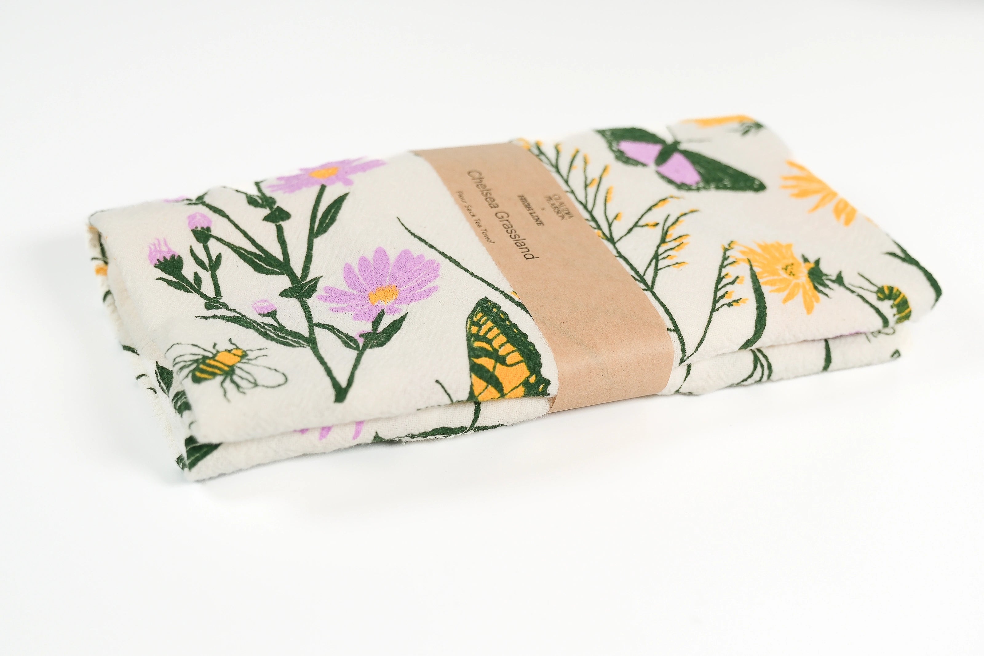Claudia Pearson x High Line Chelsea Grassland tea towel, folded and wrapped in a kraft paper band. The flour sack cotton tea towel is covered in illustrations of butterflies and flowers that populate the High Line in green, yellow, and violet.