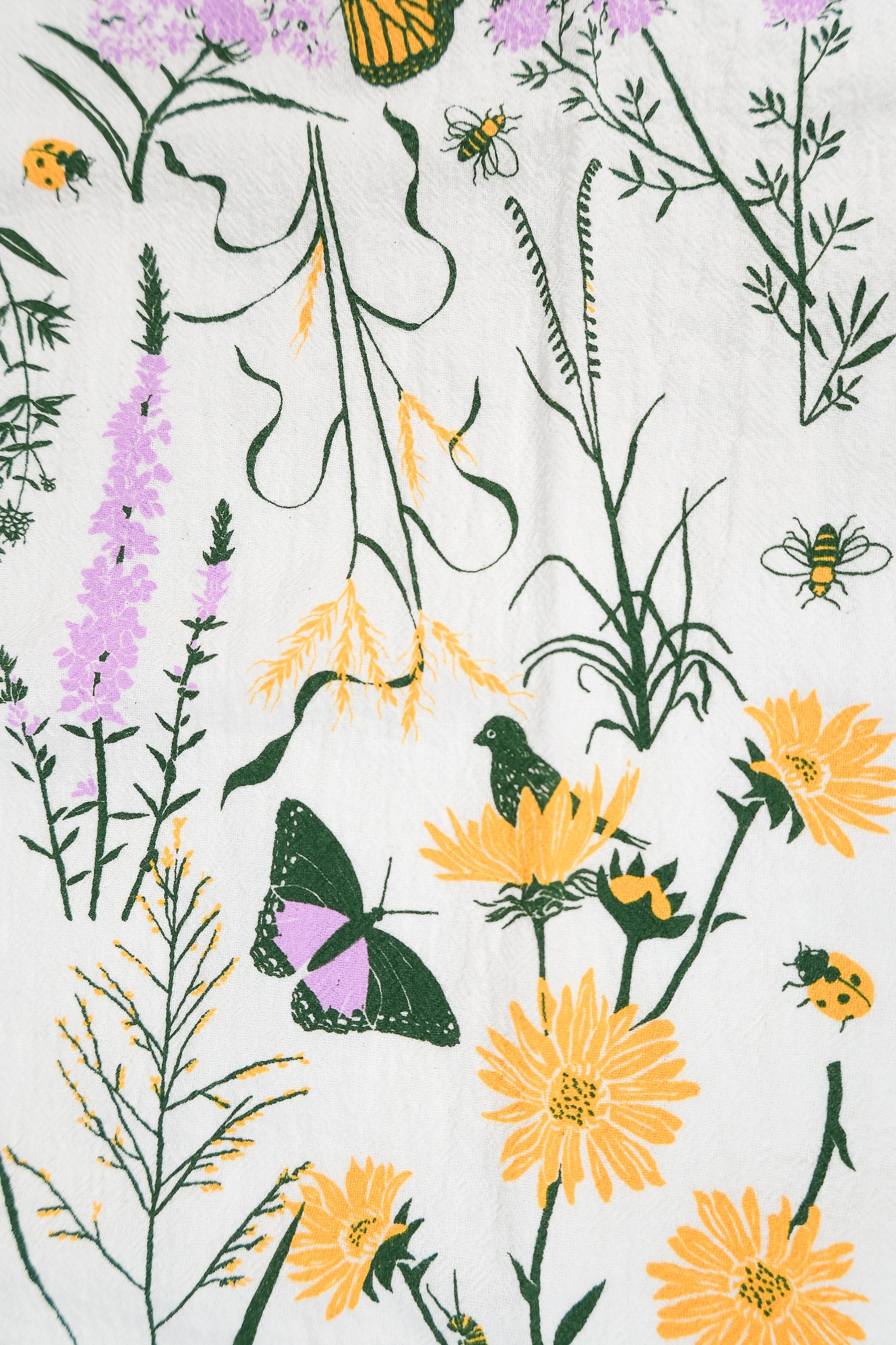 Claudia Pearson x High Line Chelsea Grassland tea towel in detail. The flour sack cotton tea towel is covered in illustrations of the flowers and grasses that grow in the Chelsea Grassland area of the High Line in pale purple, deep green and yellow.