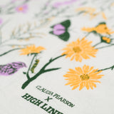 Claudia Pearson x High Line Chelsea Grassland tea towel in closeup. The flour sack cotton tea towel is covered in illustrations of the flowers and grasses that grow in the Chelsea Grassland area of the High Line in pale purple, deep green and yellow.