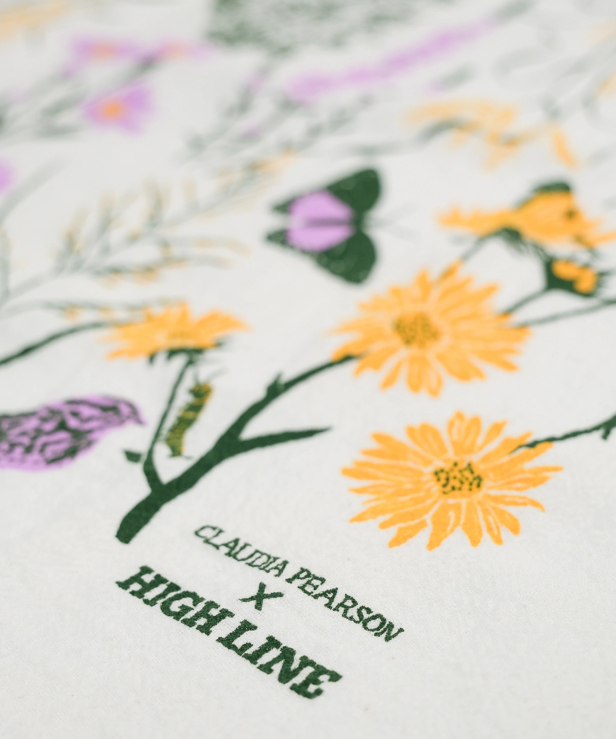 Claudia Pearson x High Line Chelsea Grassland tea towel in closeup. The flour sack cotton tea towel is covered in illustrations of the flowers and grasses that grow in the Chelsea Grassland area of the High Line in pale purple, deep green and yellow.