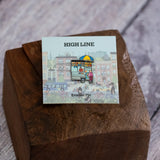 Street Vendor enamel pin—NYC street food cart—shown against the backing card and resting on a wood block.