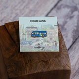 The MTA Bus enamel pin shown against the backing card and sitting on a wood block.