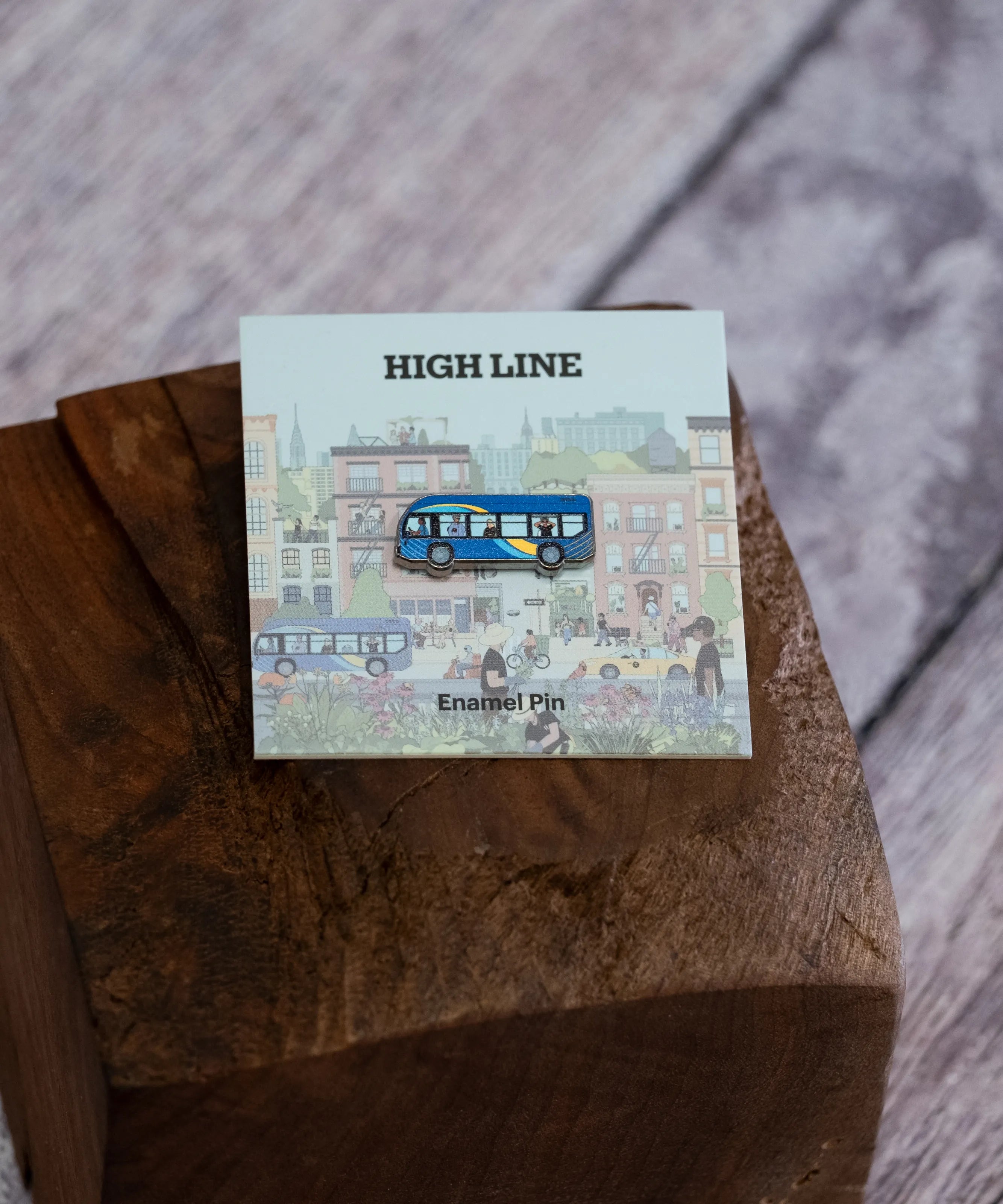 The MTA Bus enamel pin shown against the backing card and sitting on a wood block.
