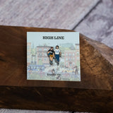 The Couple enamel pin—a couple walking down the street and talking, as illustrated by Jiaqi Wang— shown against the backing card and resting on a wood block.