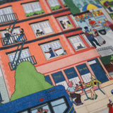 Close-up of the Community in the Sky Tote—an NYC building with people visible in the apartments, an MTA bus, and other illustrations of NYC life are visible.