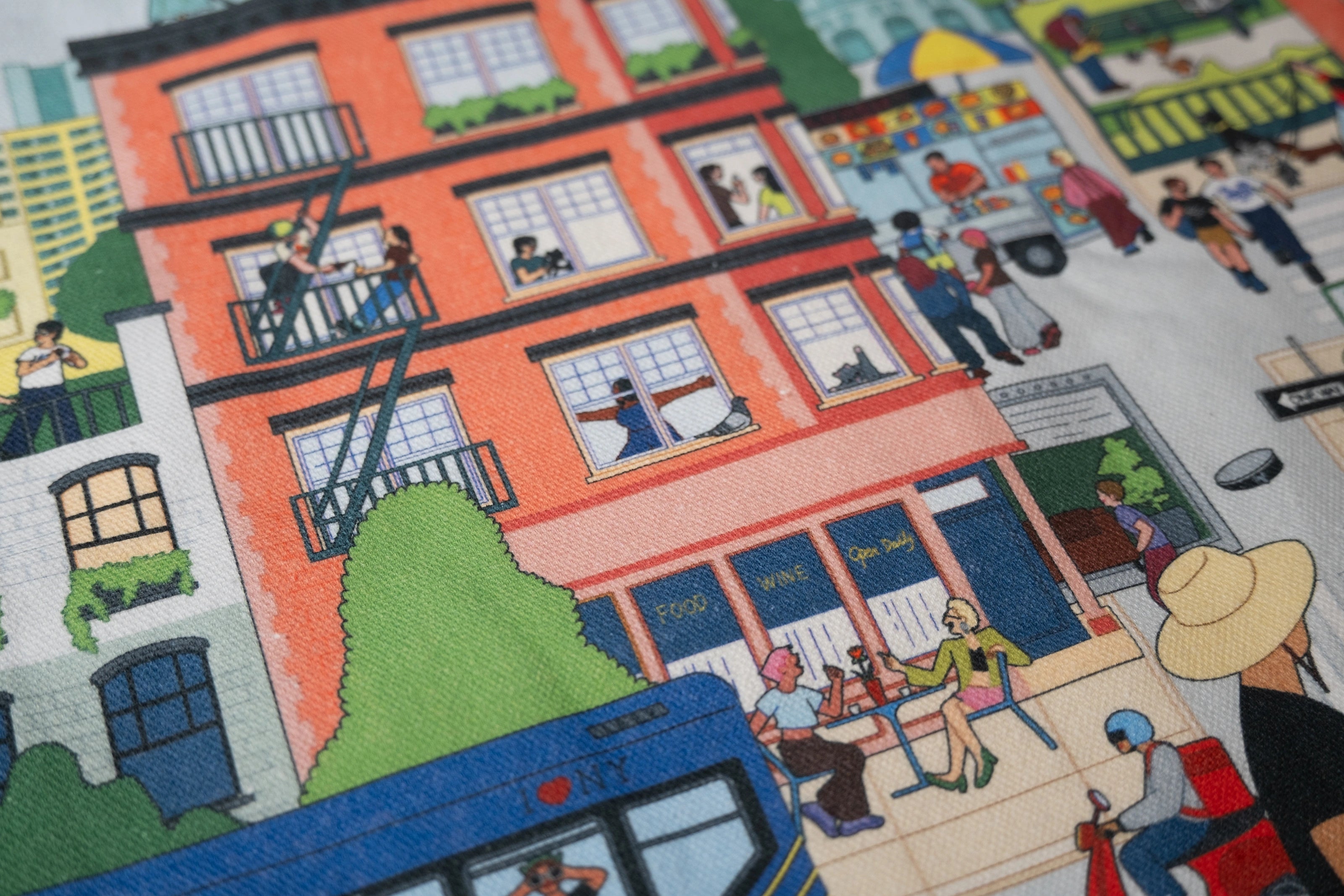 Close-up of the Community in the Sky Tote—an NYC building with people visible in the apartments, an MTA bus, and other illustrations of NYC life are visible.
