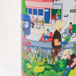 Closeup of stainless steel water bottle with a colorful design and 'High Line' branding on a blue background with wooden lid. Features the Nature in the City illustration by Jiaqi Wang.