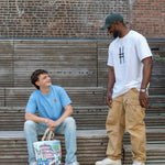 Two men talking on the High Line, one with the Community in the Sky Tote.