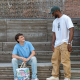 Two men talking on the High Line, one with the Community in the Sky Tote.