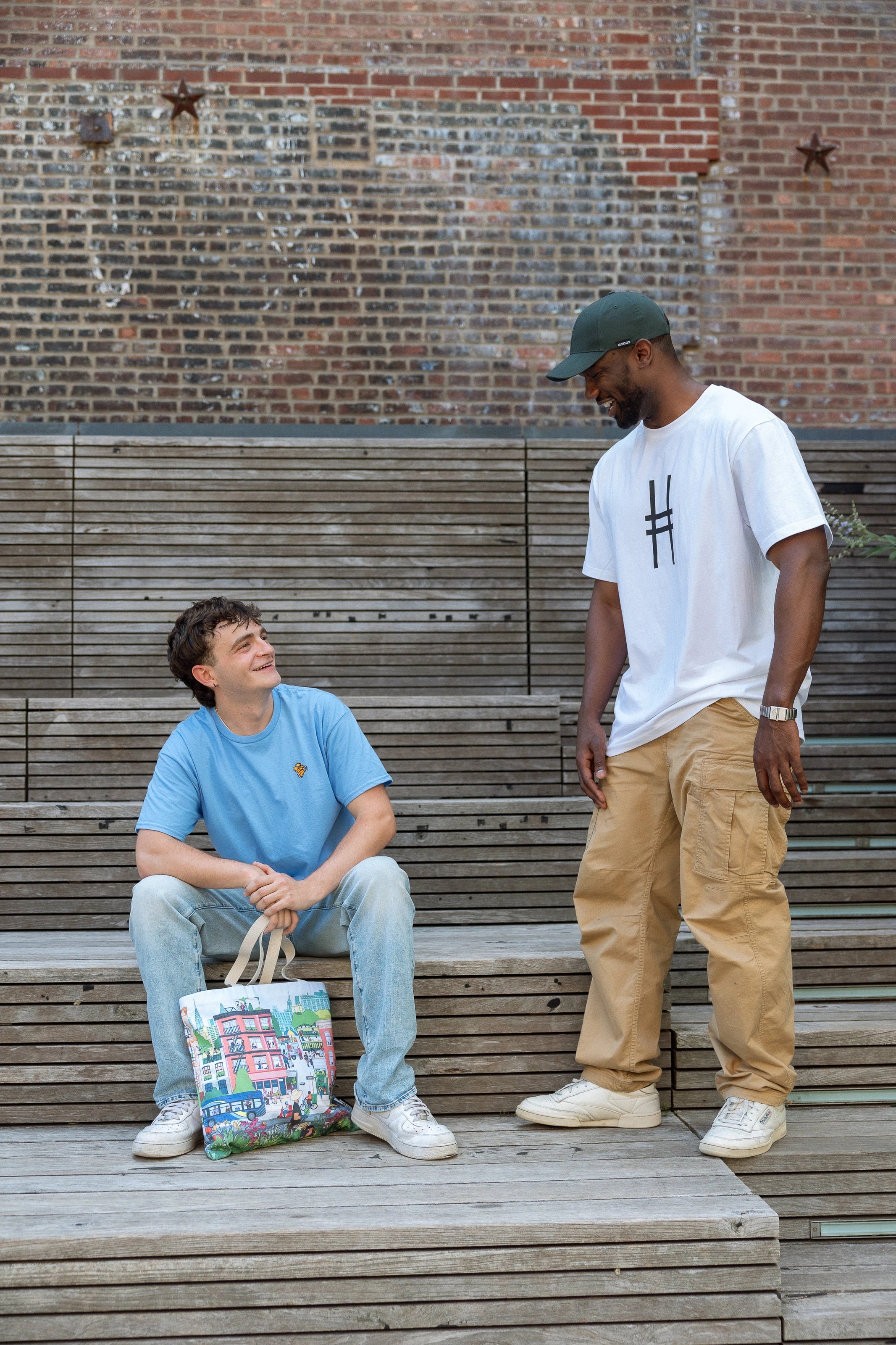 Two men talking on the High Line, one with the Community in the Sky Tote.