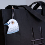 A close-up of the Dinosaur pigeon head bag charm made from PVC against the Park in the Sky black cotton canvas tote.