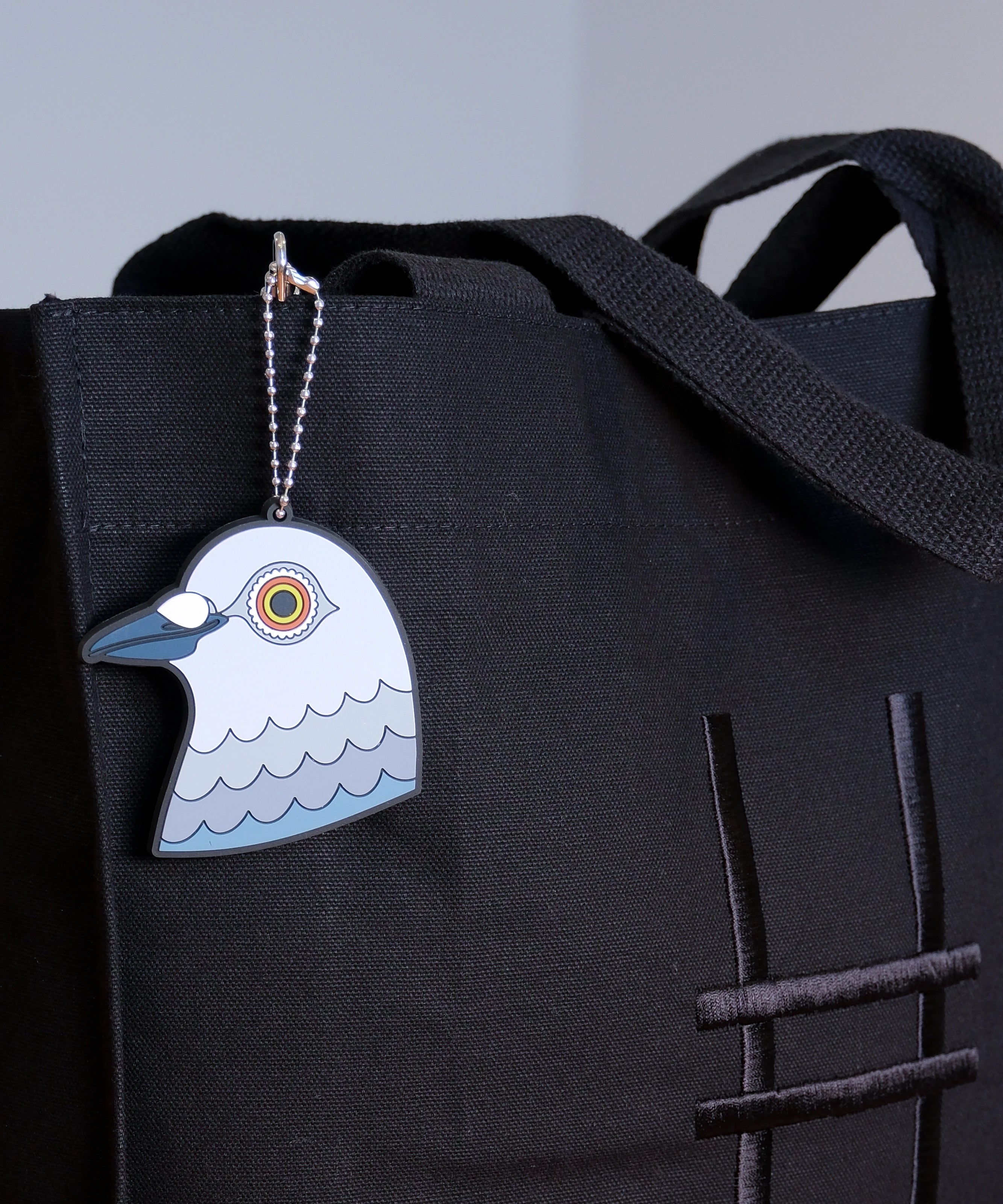 A close-up of the Dinosaur pigeon head bag charm made from PVC against the Park in the Sky black cotton canvas tote.