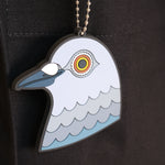 A close-up of the hanging pigeon head bag charm made from PVC against the Park in the Sky black cotton canvas tote.