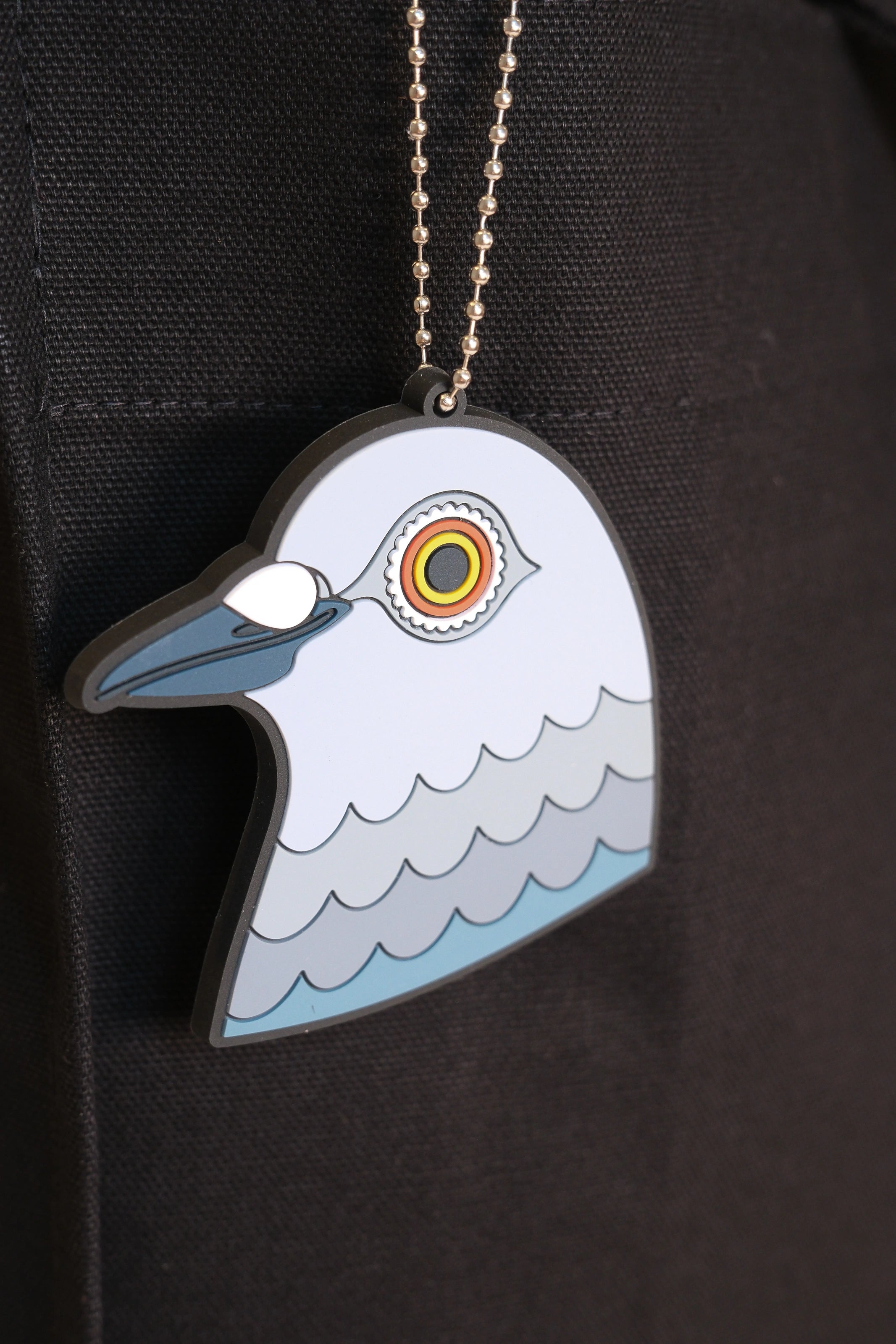 A close-up of the hanging pigeon head bag charm made from PVC against the Park in the Sky black cotton canvas tote.