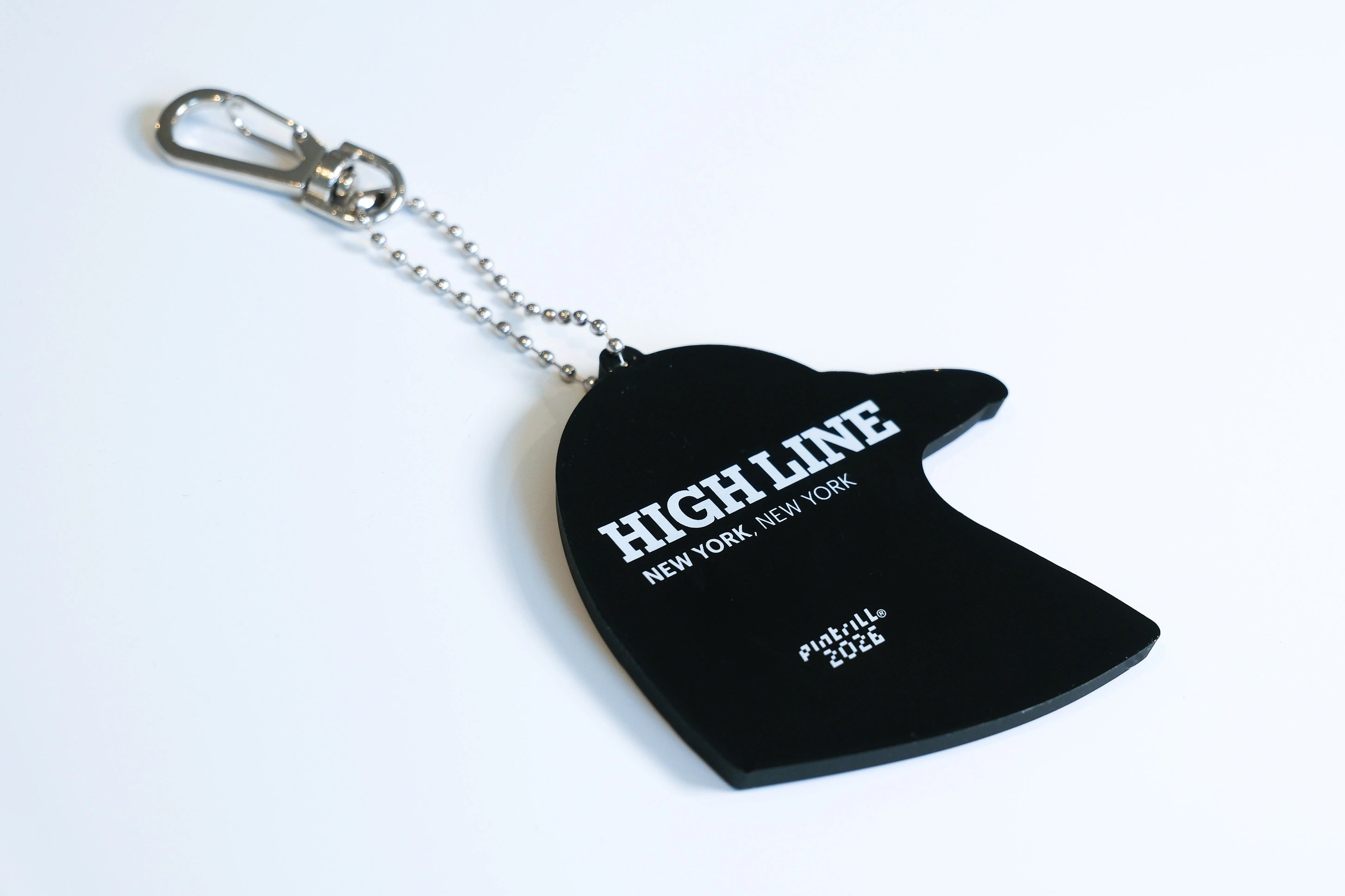 The backside of the Dinosaur-inspired pigeon head bag charm made from PVC. The back is all black with the High Line logo and "New York, New York" in white, as well as Pintrill, the manufacturer's logo.