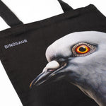 Closeup shot showing Dinosaur Tote front, with big pigeon head and "Dinosaur" screen-printed  on a black tote.