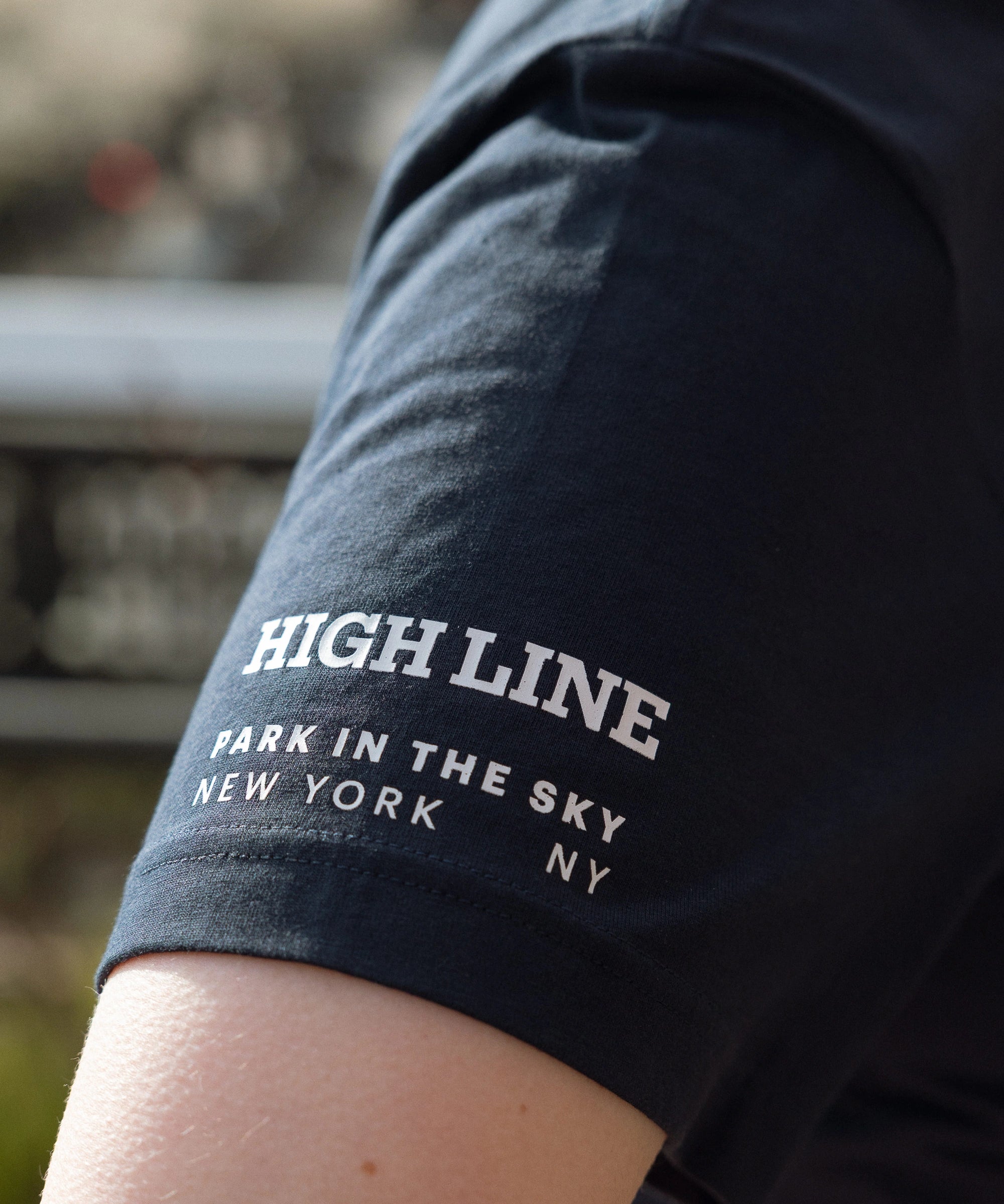 Sleeve detail. High Line wordmark and park in the sky tagline in white against the navy tee.