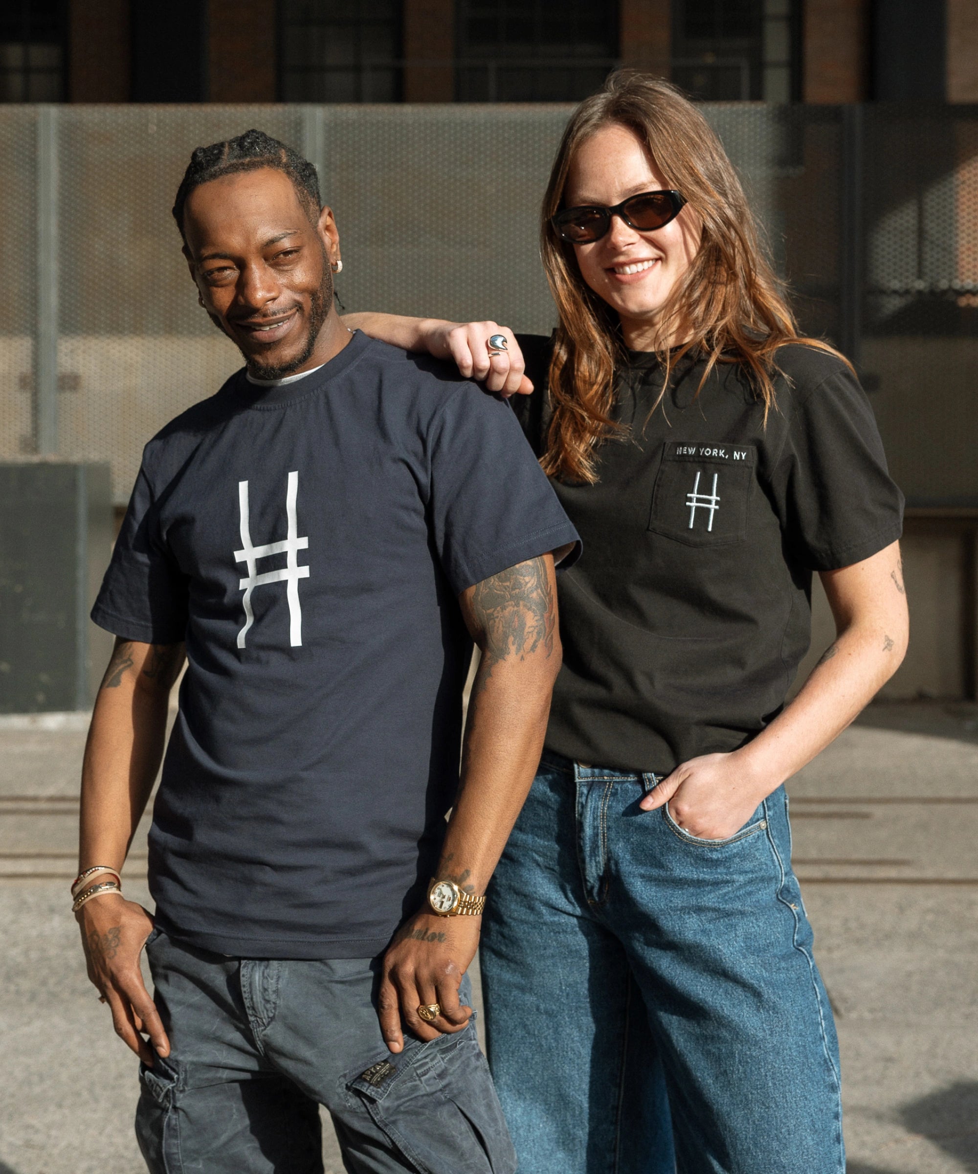 Two people, one wearing the Big Icon Tee in navy, and the other wearing the High Line Embroidered Pocket Tee.