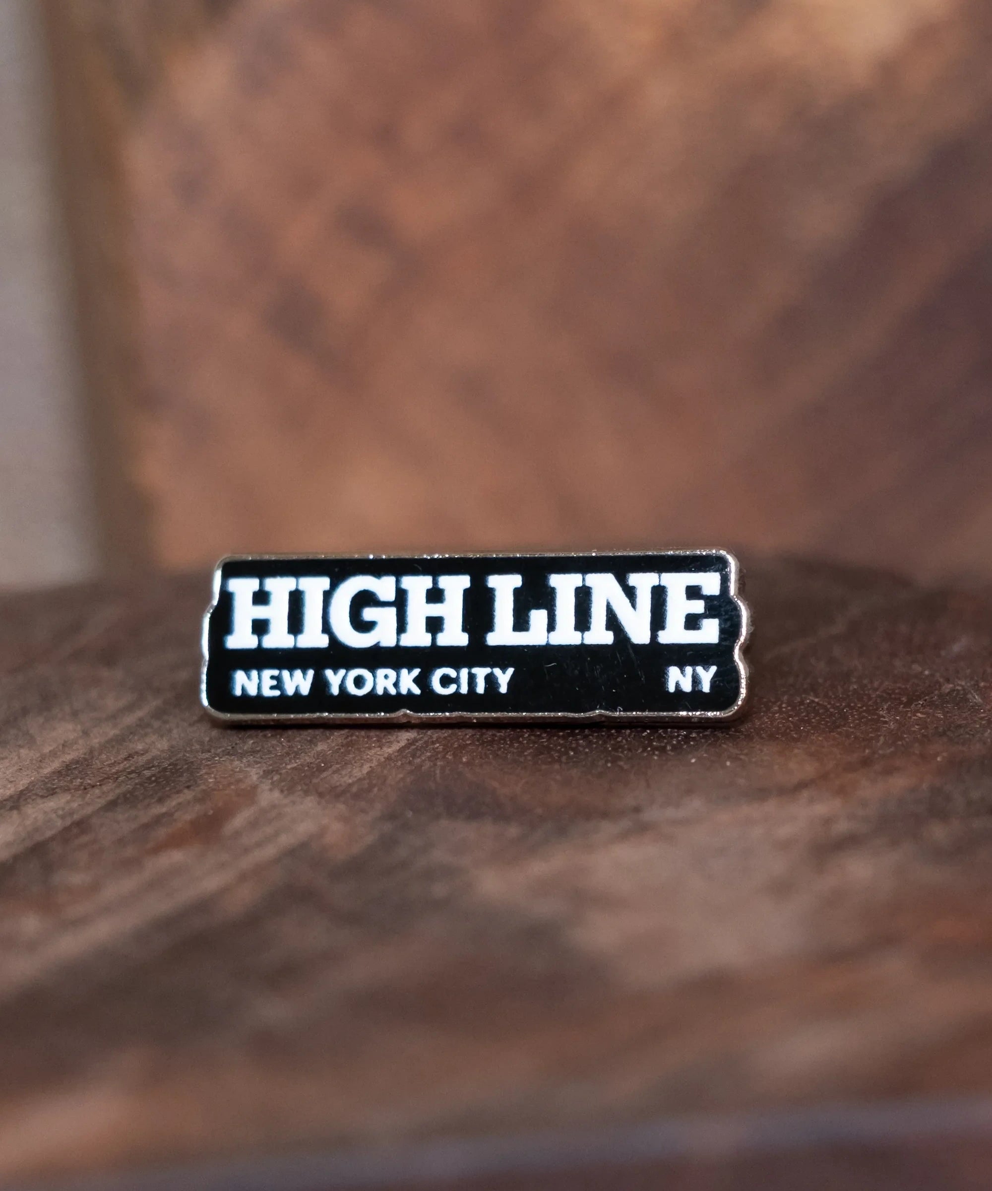 High Line Enamel Pin sitting on a dark wood block.