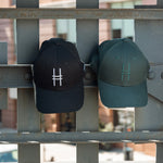 Both High Line Icon Caps side by side hanging off of the historic High Line railing.