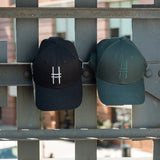Both High Line Icon Caps side by side hanging off of the historic High Line railing.