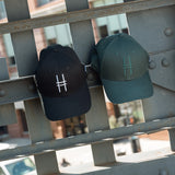 Both High Line Icon Caps hanging off of the historic High Line railing.