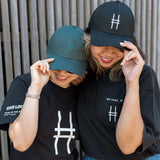 Two women, each wearing a High Line Icon Cap and t-shirt and smiling.