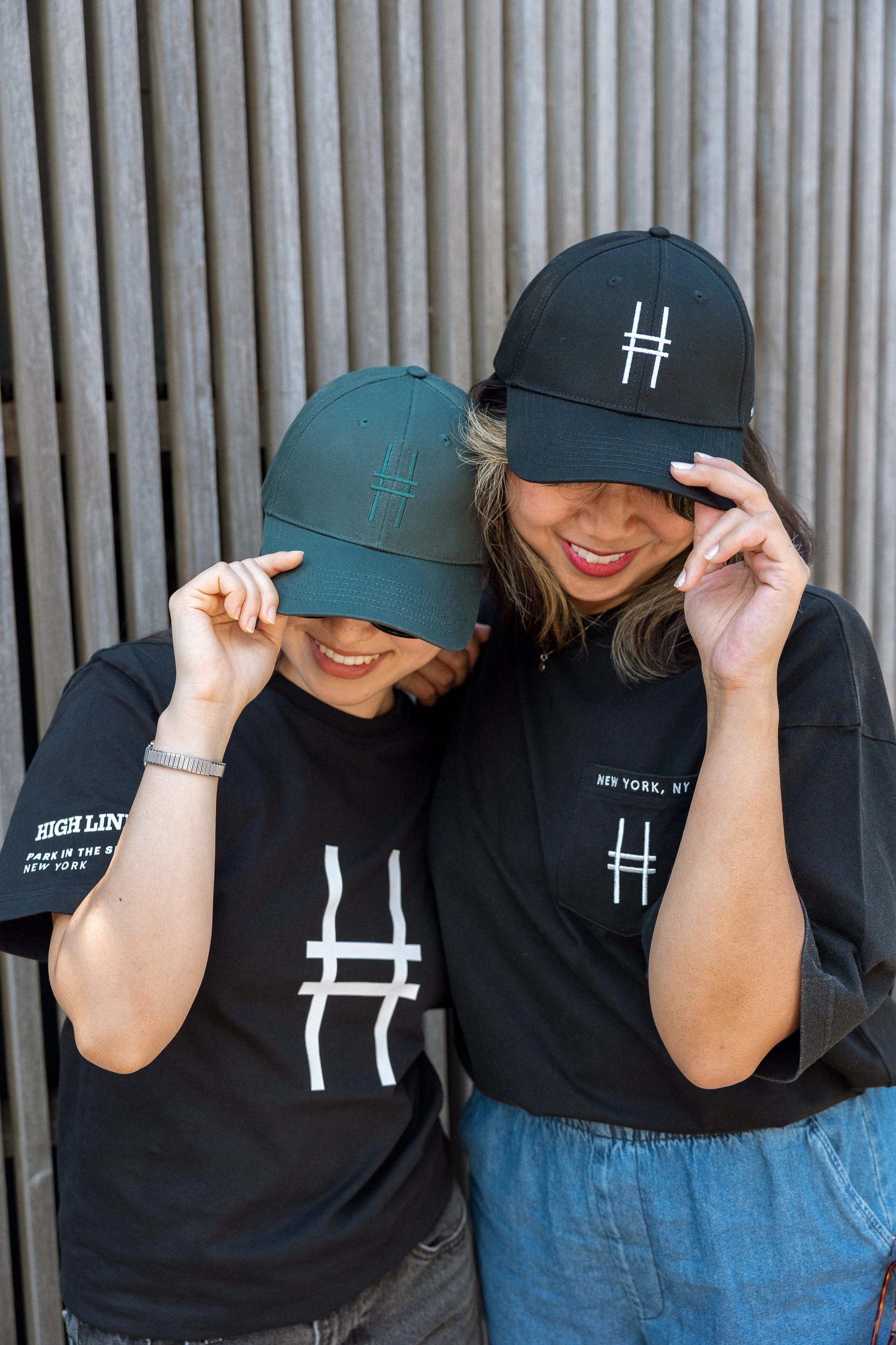 Two women, each wearing a High Line Icon Cap and t-shirt and smiling.