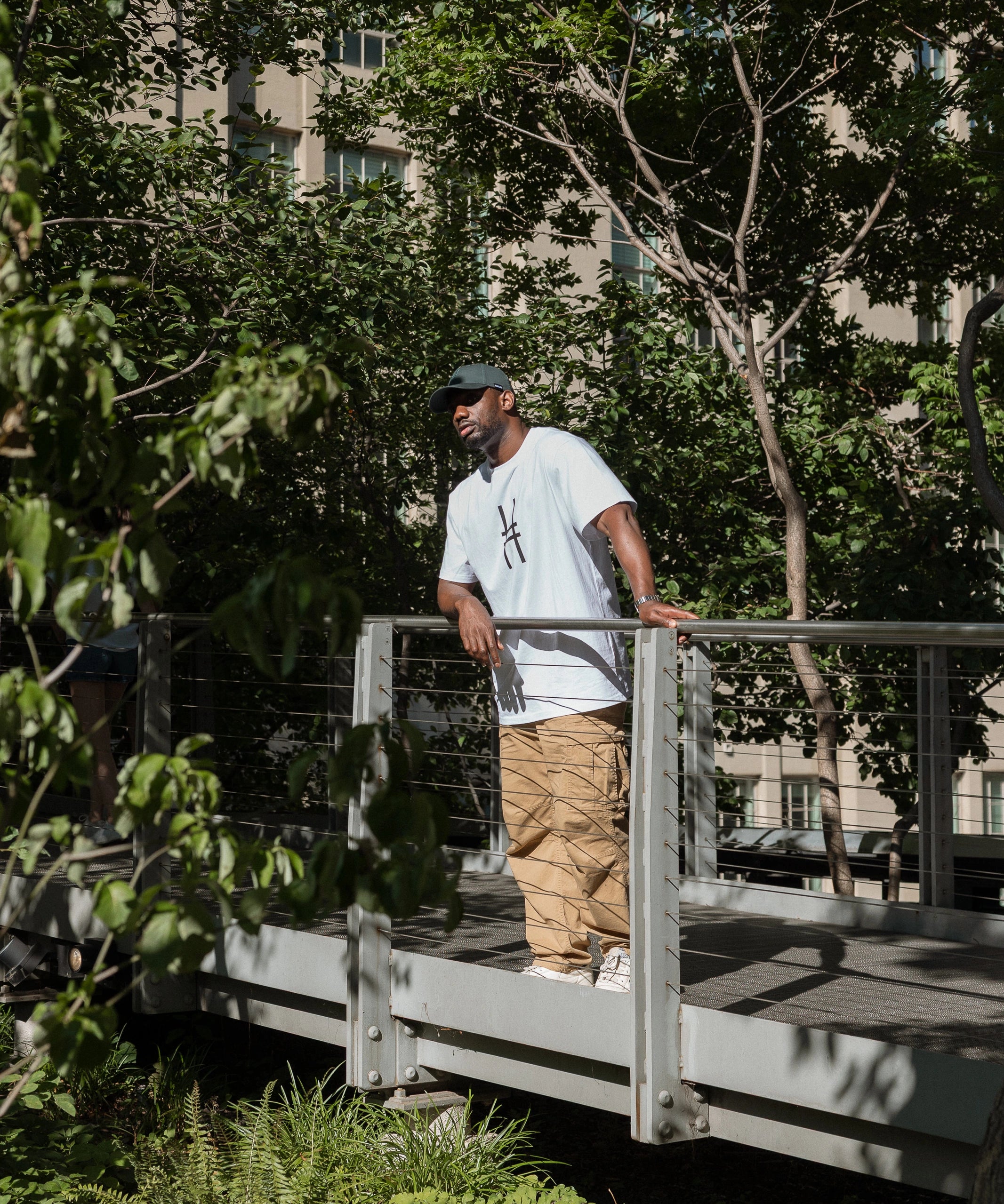 Man wearing the Big Icon Tee in white and High Line Icon Cap standing amidst the trees on the High Line.