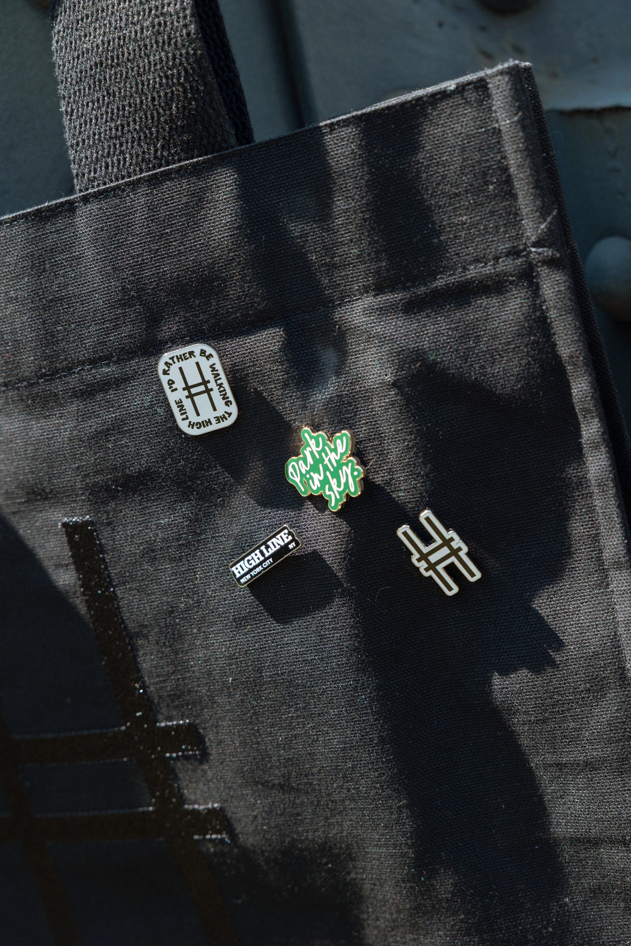 All the High Line Icon collection pins on the Park in the Sky Tote against the High Line railing.