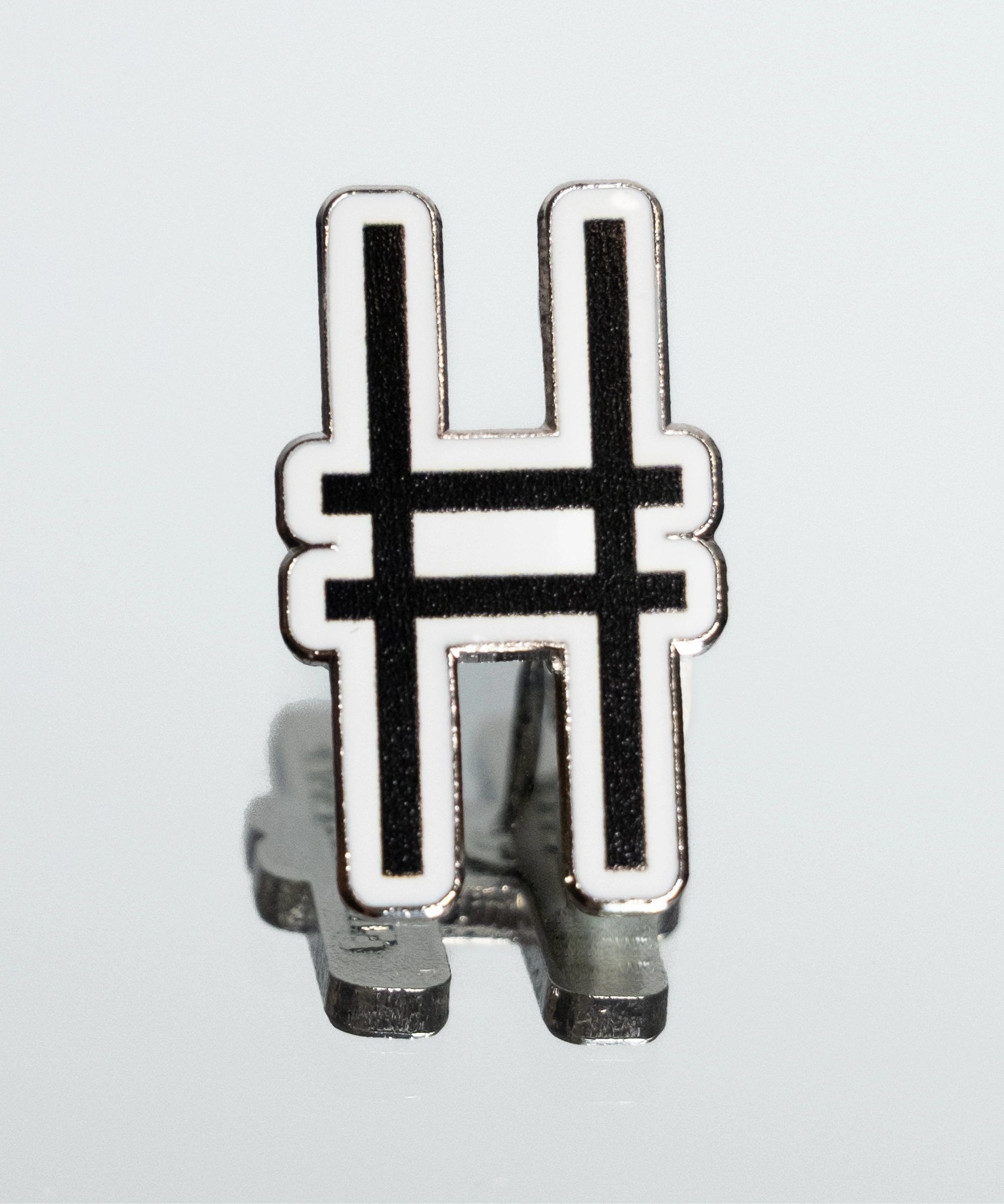 High Line Icon Enamel Pin—the High Line railroad track "H" logomark/icon in black set against white enamel—shown on a mirrored surface.