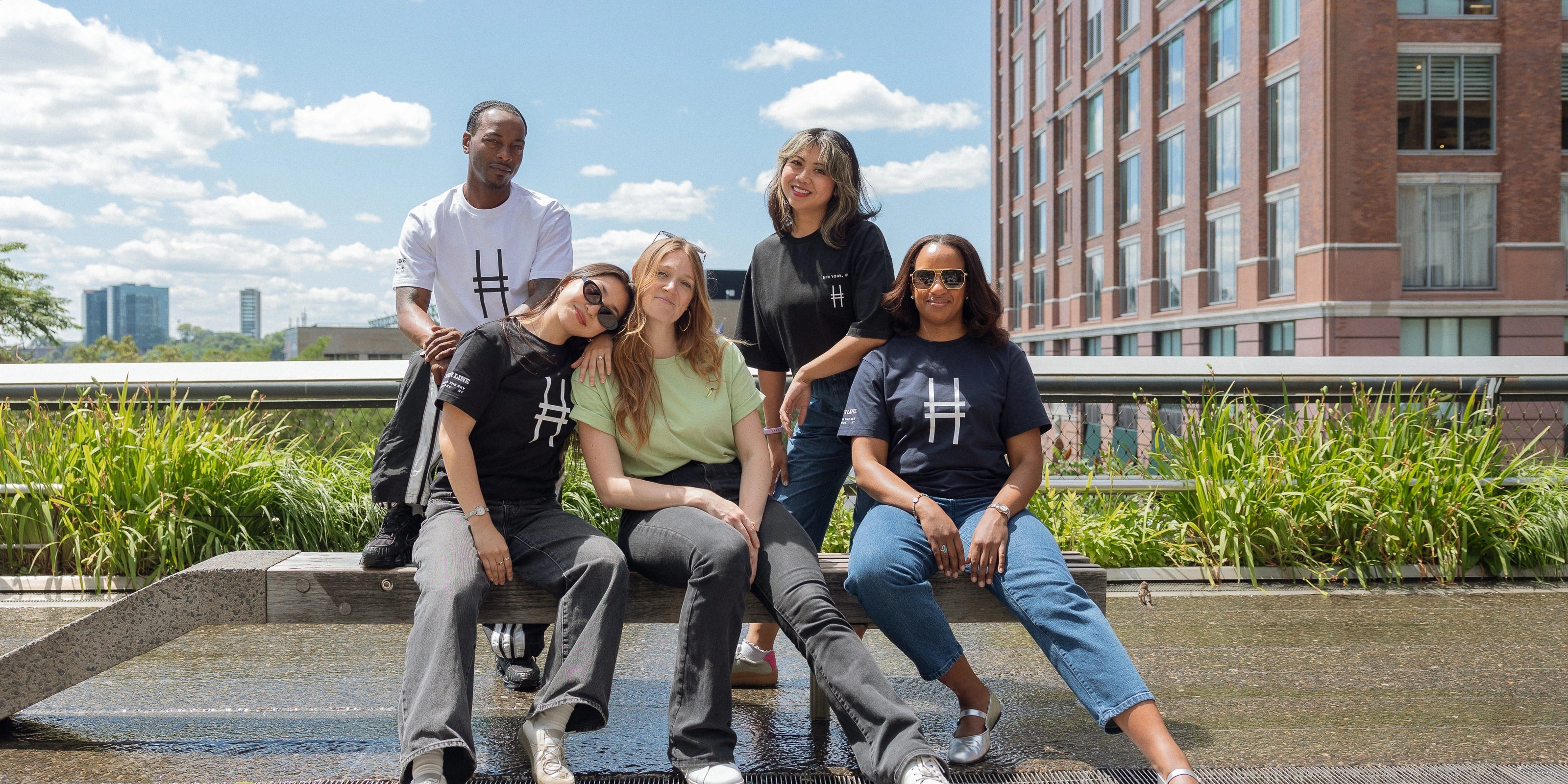 Five people, each wearing High Line apparel, sit on the sun deck on the High Line.
