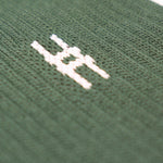 Close-up of the High Line Socks in Ivy—dark green ribbed knit fabric with an intarsia small white High Line train-track "H" icon.