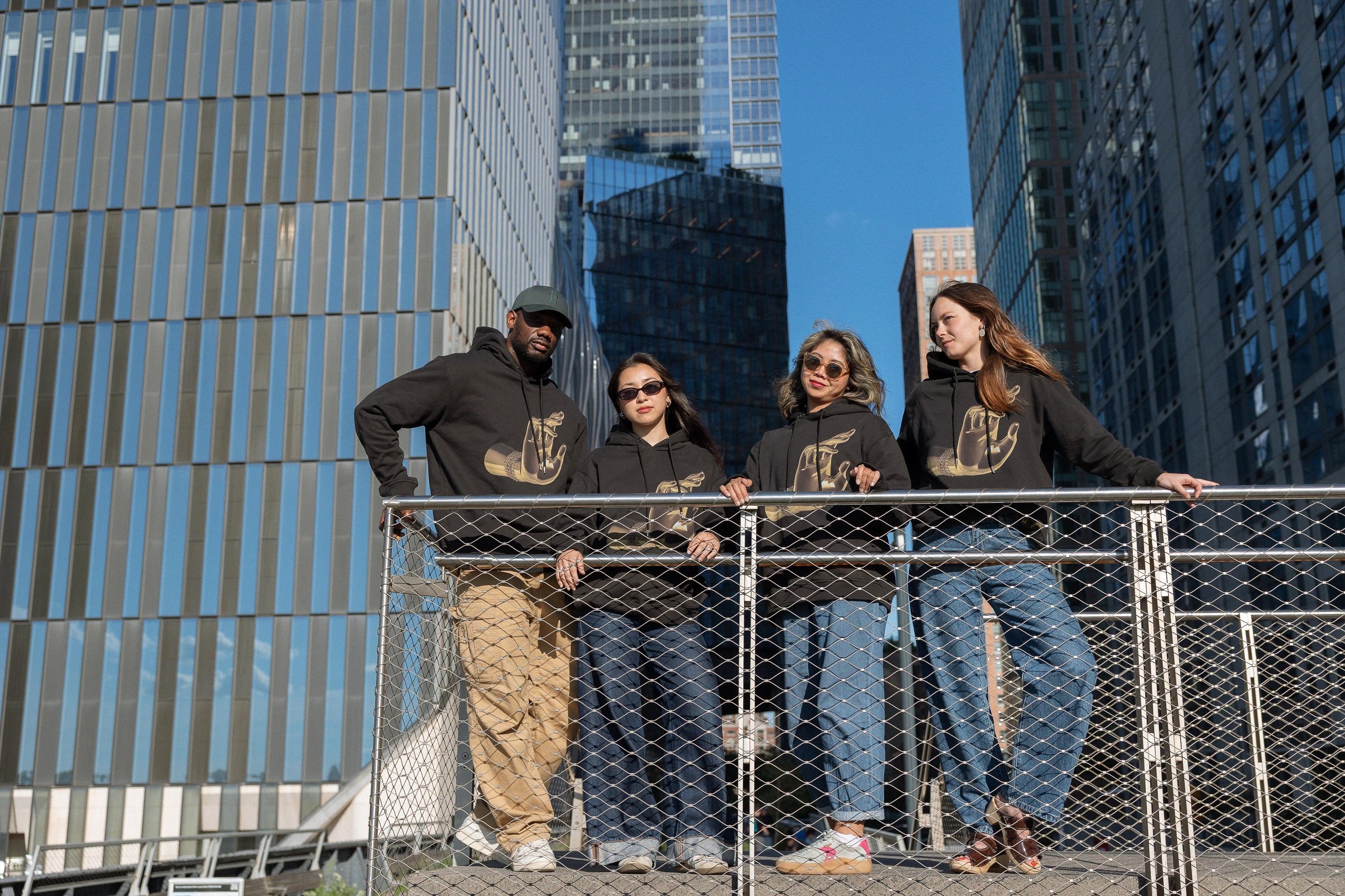 Four people, each wearing The Light That Shines... Hoodie stand on the steps on the northern end of the High Line.